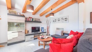 A modern living room with a sofa, red cushions, a coffee table, and a TV. There are wooden beams on the ceiling, a bookshelf, and a decorative vase with branches. - Finca Can Daniel, pool, A/C, Wifi, close to the beach 4 km, quiet location, 3 bedrooms. (Pollenca)
