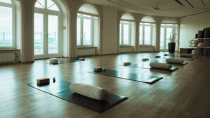 Une pièce spacieuse dotée de planchers en bois, de grandes fenêtres en arc de cercle et de tapis de yoga disposés pour la pratique.