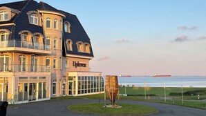 Un grand immeuble à plusieurs étages, avec une enseigne « Upleven » bien visible, une façade en verre et une vue sur la mer.