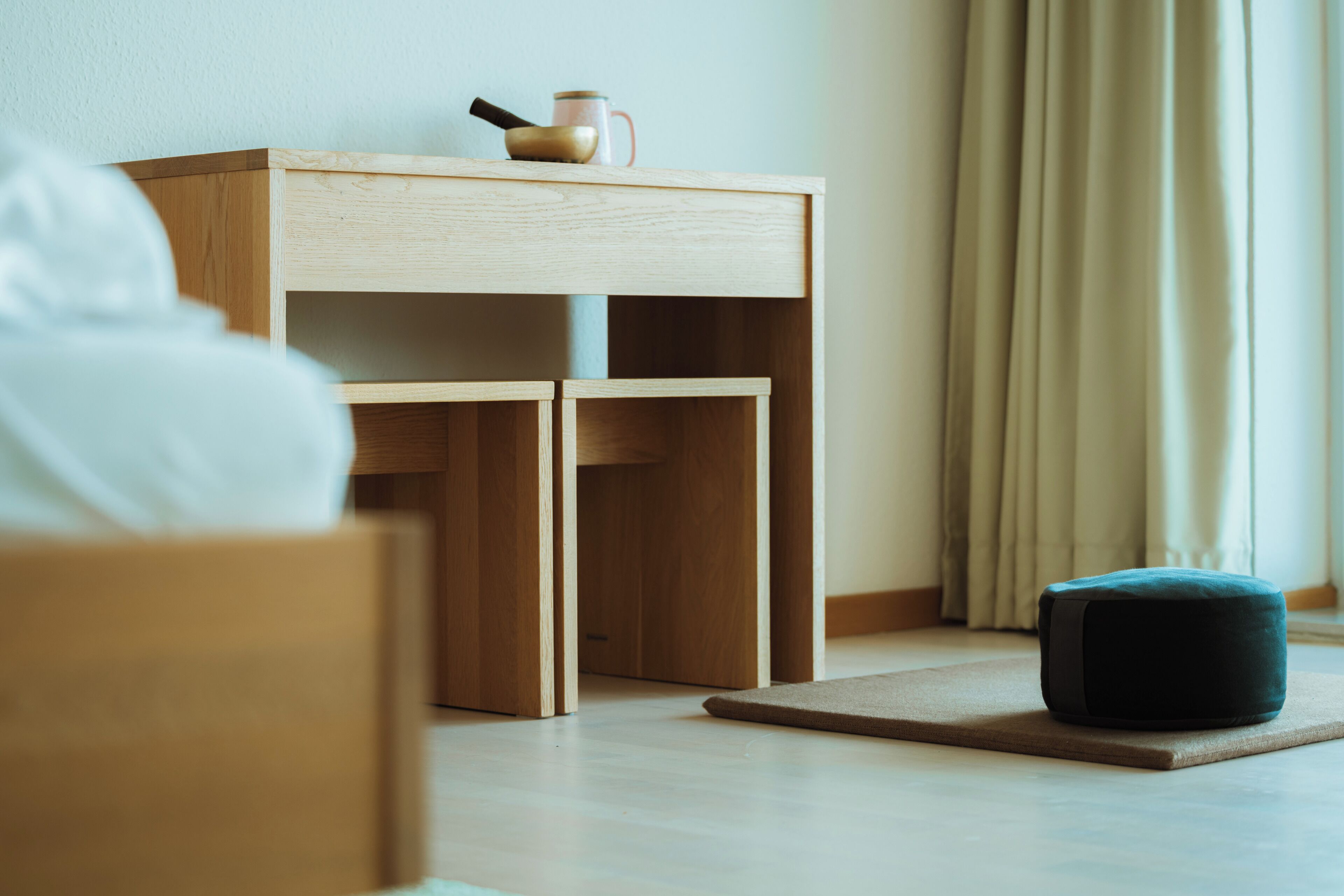 A minimalist room with a wooden nightstand, a small table, and a dark ottoman.