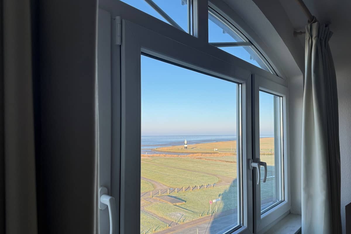 A window with a view of a coastal landscape, including a lighthouse and open fields.