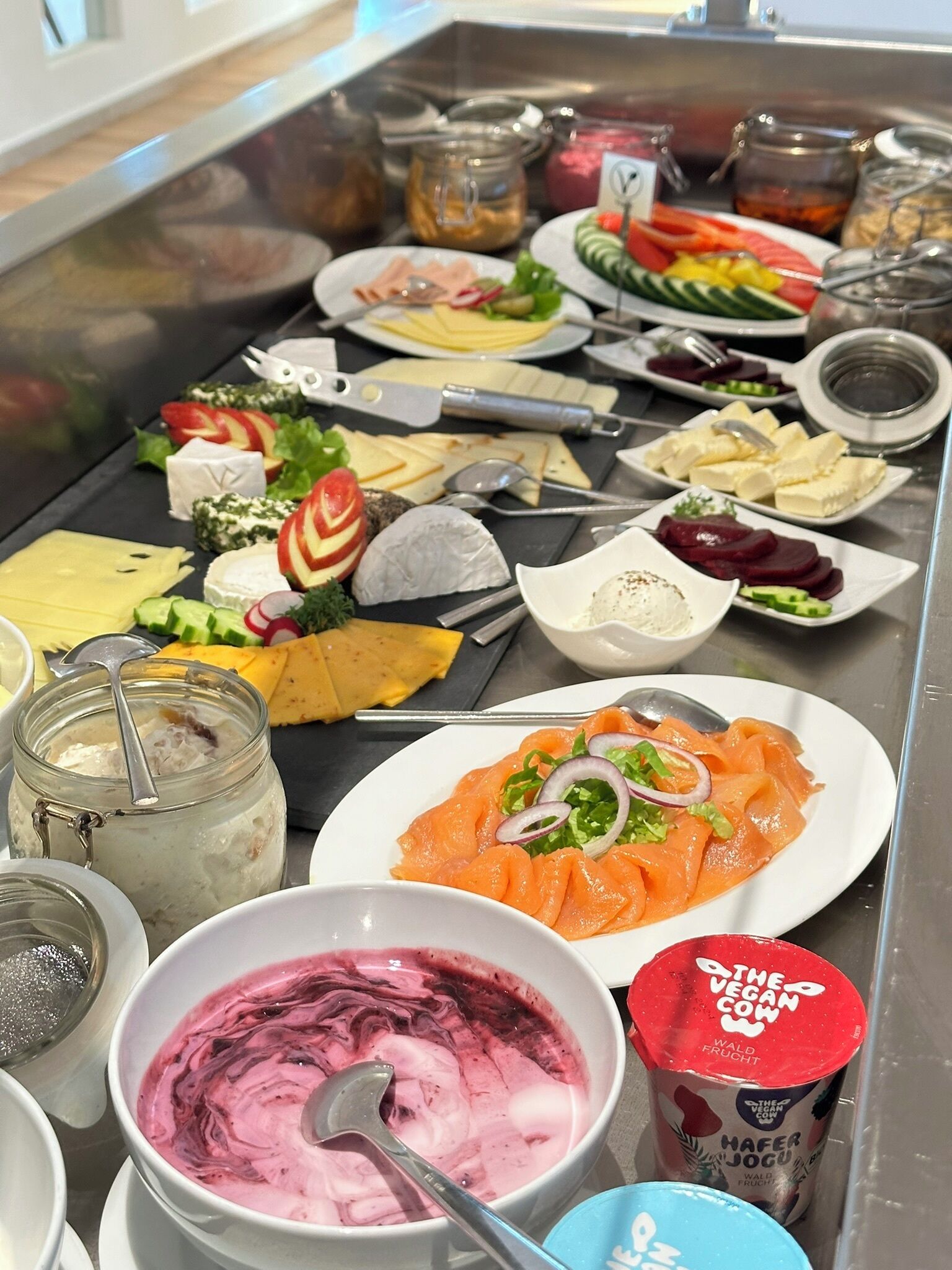 Un buffet proposant une variété d’aliments, notamment du fromage, du saumon fumé et un bol de smoothie rose.