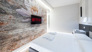 Een moderne hotelkamer met een groot bed, een bevestigde televisie met het Netflix-logo, en een gestructureerde wand.