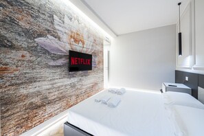 Ein modernes Hotelzimmer mit einem großen Bett, einem an der Wand befestigten Fernseher mit dem Netflix-Logo und einer strukturierten Wand.