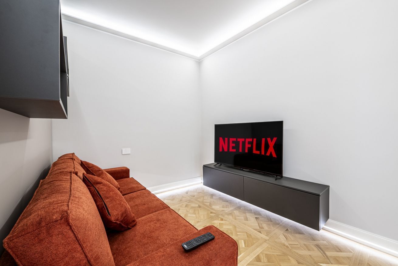 A modern living room with a sofa, a TV mounted on a wall, and a remote control on the sofa.
