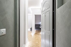 A hallway with a light switch on the wall, a wooden floor, and a door leading to another room. - Beccaria - Luxury Apartment in Florence (Florence)