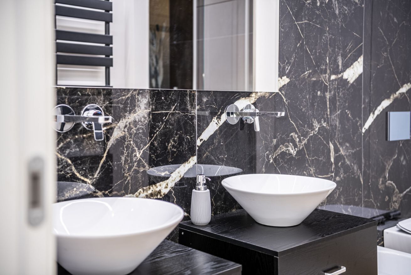 A modern bathroom with two white vessel sinks, a black marble backsplash, and a large mirror.