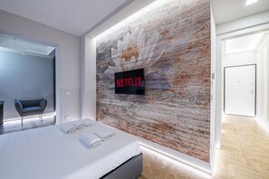 Une chambre d’hôtel moderne avec un grand lit, un téléviseur fixé au mur et un mur à la texture rustique.