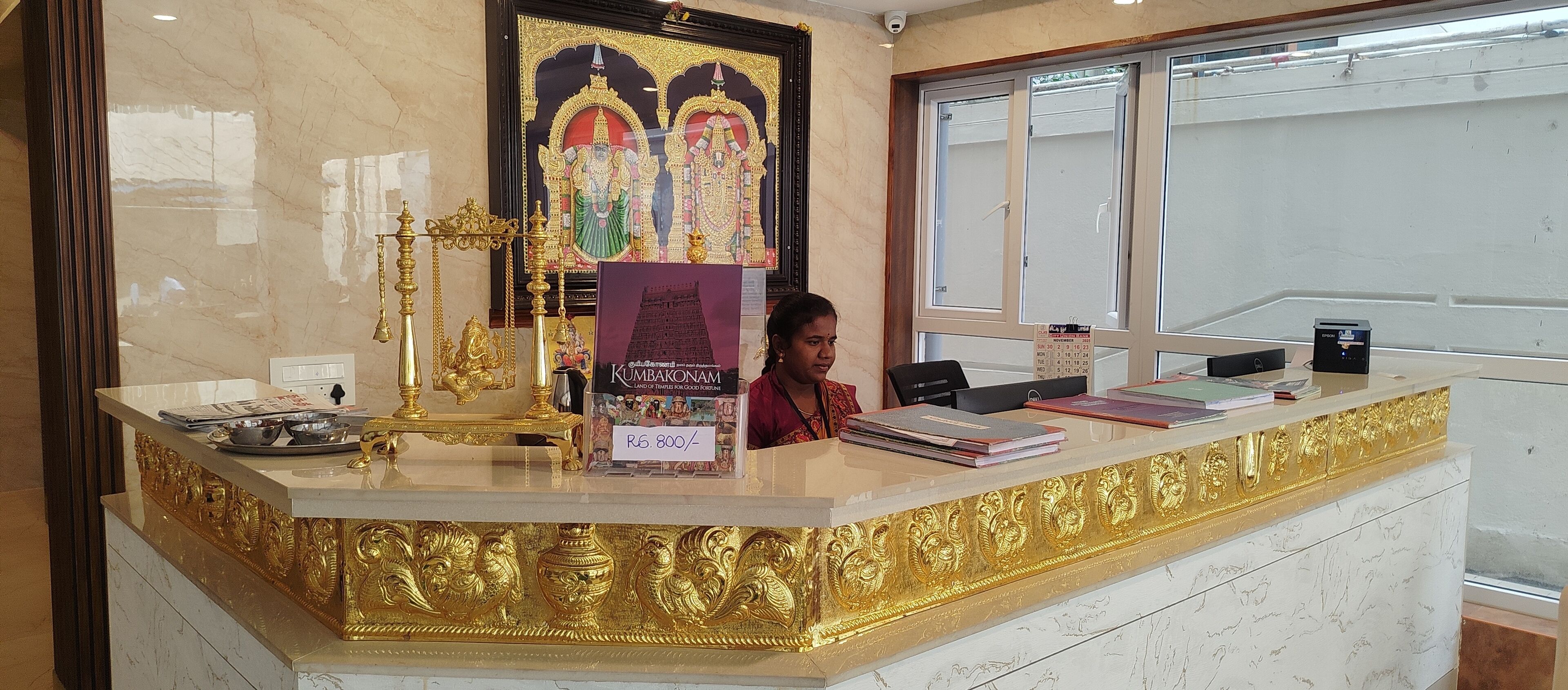 A reception desk with a gold and white marble design, a framed religious painting, and a sign indicating the price of a book.