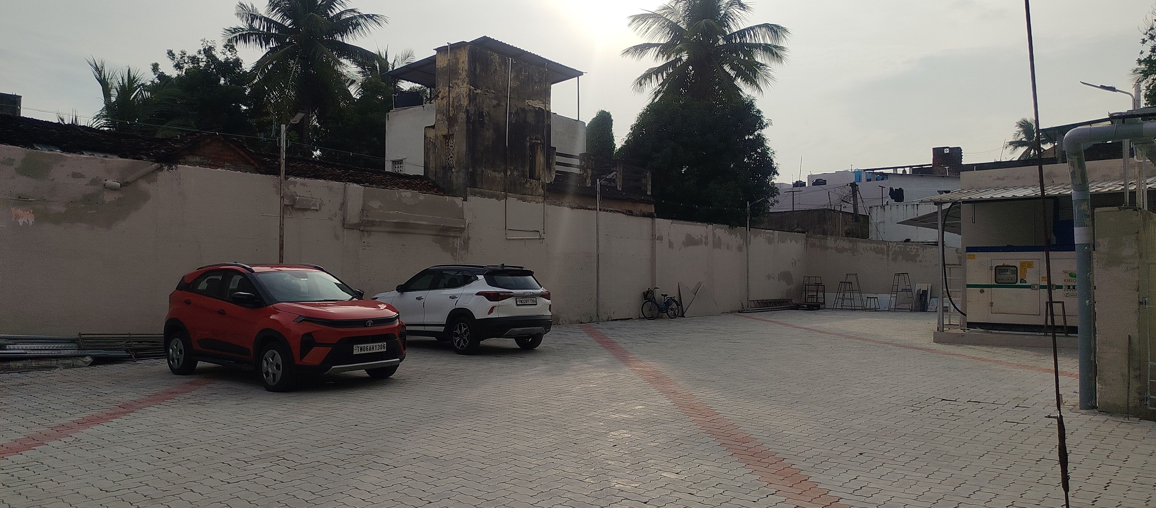 Un estacionamiento con dos coches, un edificio blanco y palmeras al fondo.
