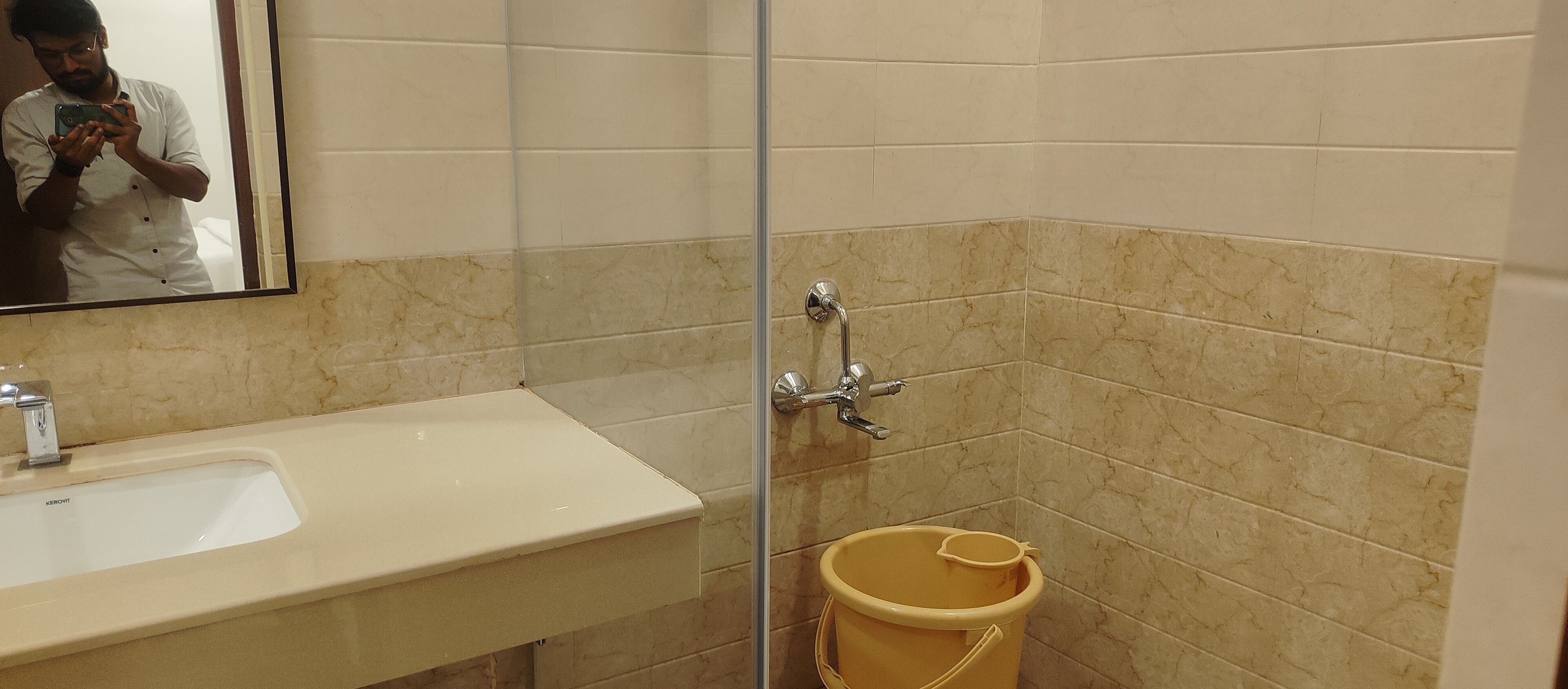 A bathroom with a sink, mirror, shower, and a yellow bucket.