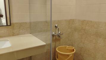 Baño con lavamanos, espejo, ducha y un cubo amarillo.