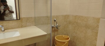 Baño con lavamanos, espejo, ducha y un cubo amarillo.