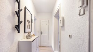 A narrow hallway with a white door at the end, a white cabinet with decorative items, and a wall-mounted telephone. - Apartment 'Horsti' with Wi-Fi (Timmendorfer Strand)