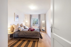 Une chambre à coucher avec un lit, une table de chevet avec une lampe, une fenêtre avec des rideaux et une porte.