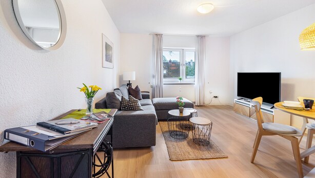 A modern living room with a sofa, a dining table, a TV, and a large window. - Apartment 'Horsti' with Wi-Fi (Timmendorfer Strand)