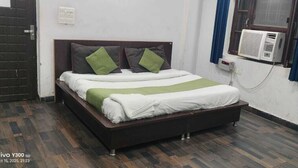 A bed with a wooden frame, white bedding, and green and gray pillows. - Hotel Rameshwaram Inn (Rishikesh)