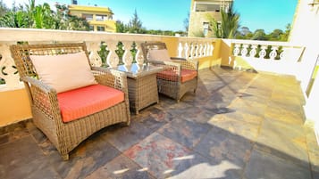 A balcony with wicker furniture and a glass-top table.