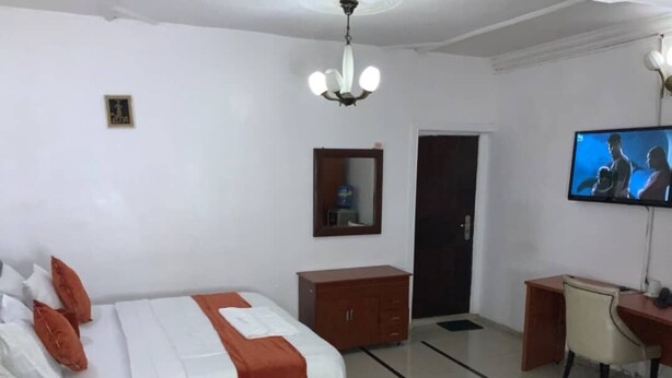 Habitación de hotel con cama, escritorio, silla, televisor, armario y puerta.