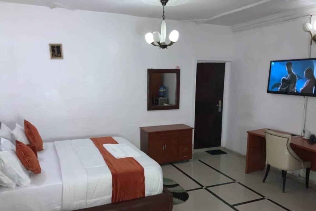 A hotel room with a bed, a desk, a chair, a television, a wardrobe, and a door.