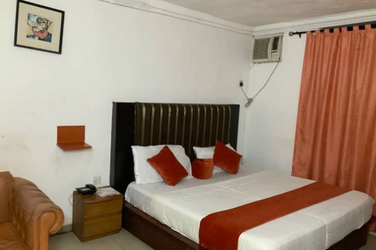 A bedroom with a bed, a nightstand, a chair, a picture on the wall, and a window with curtains.