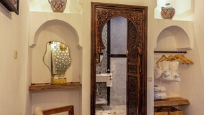 A traditional room with an ornate wooden door, a mirror with a decorative frame, a small seating area, and a shelf with towels and a tray of food. - Elegant Riad Musée: Authentic Marrakech Charm in the Medina (marrakech)
