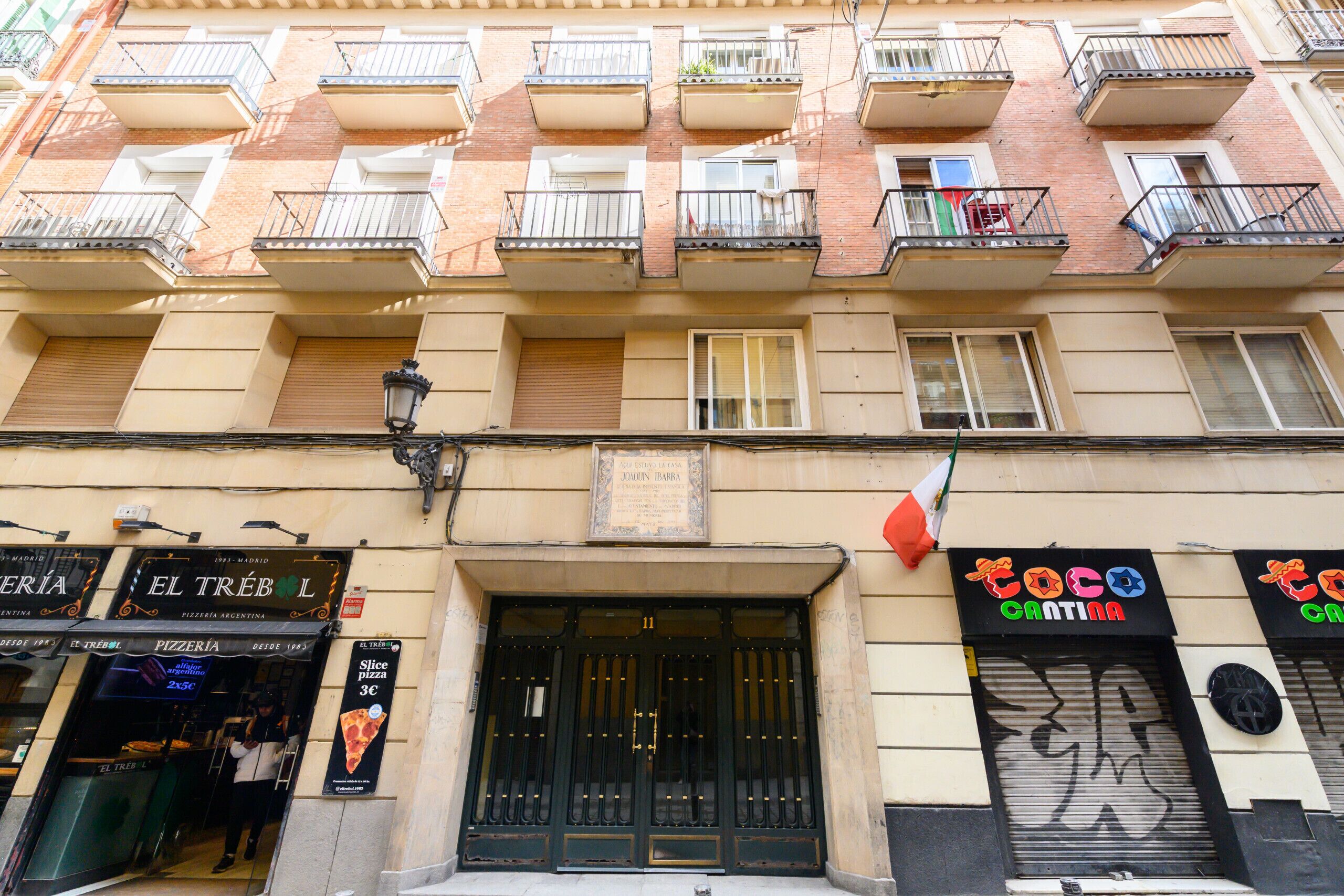 A multi-story building with a pizzeria on the ground floor, balconies with railings, and a sign for 'Coco Cratina'.