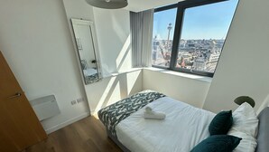 Une chambre d’hôtel avec un lit, une fenêtre donnant sur la ville, un miroir et une porte.