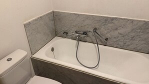 Ein Badezimmer mit einer weißen Badewanne, einer Toilette und Marmorwänden.