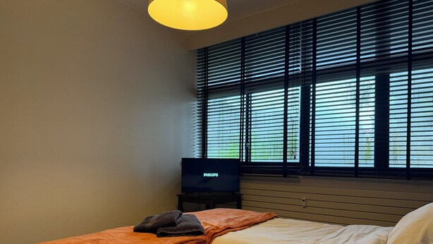 Ein Hotelzimmer mit Bett, Fernseher und einem Fenster mit Jalousien.