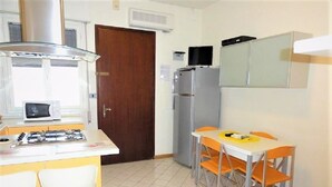 A compact kitchen with a gas stove, microwave, refrigerator, and a small dining area with chairs and a table. - Central flat with terrace and parking (Bibione)