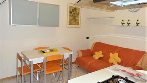 A compact kitchen with a gas stove, a dining table with chairs, and a sofa. - Central flat with terrace and parking (Bibione)