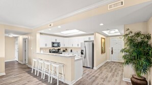 Una cocina moderna con armarios blancos, electrodomésticos de acero inoxidable y una isla central con taburetes de bar.