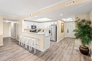 A modern kitchen with white cabinets, stainless steel appliances, and a central island with bar stools. - Royale Palms 205 3 Br Oceanview in Kingston, Pool (Myrtle Beach)