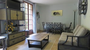 Een woonkamer met een bank, een eettafel met stoelen, een salontafel en een kast met bloemen.