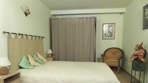 Een slaapkamer met een bed, nachtkastjes, een stoel, een gordijn en een foto aan de muur.