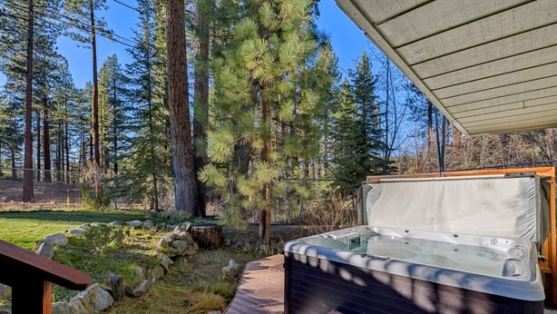 Un bain à remous sur une terrasse en bois, dotée d’un espace abrité, le tout entouré d’un paysage boisé.