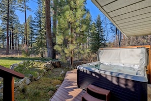 Een hottub op een houten terras met een overdekte ruimte, omgeven door een bebost landschap.