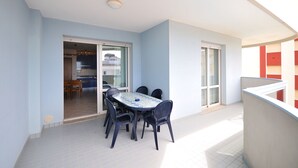 A balcony with a table and chairs, a sliding glass door leading to a kitchen, and a view of a building with red balconies. - Relax in comfort with pool and sea nearby (Bibione)