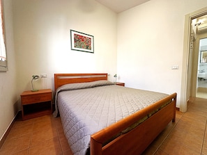 A bedroom with a bed, nightstands, a wall-mounted lamp, and a door leading to a bathroom. - Comfy villa in central location (Bibione)