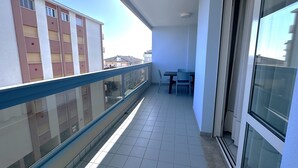 Ein Balkon mit Glasgeländer, Fliesenboden und einem Tisch mit Stühlen.