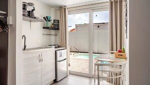 Cocina compacta con refrigerador, pileta y una pequeña mesada. Posee una puerta corrediza de vidrio que da a un espacio exterior con piscina y una mesa con sillas.