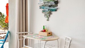 Una pequeña mesa con marco blanco, un mantel con estampado floral, dos sillas y un adorno de madera en la pared.