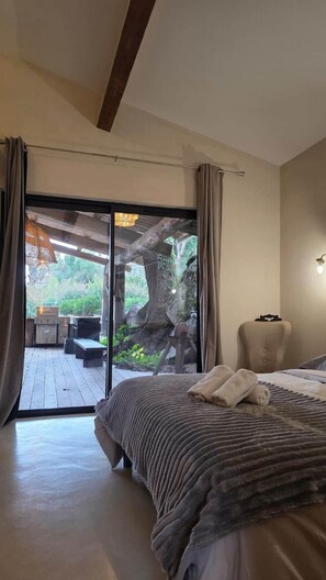 A bedroom with a large bed, a view of an outdoor deck, and a sliding glass door leading to a patio area. - Villa "Aria Natura", calm serenity heated swimming pool (Porto-Vecchio)
