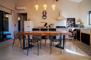 A modern kitchen with a wooden dining table, metal chairs, a stove, and hanging pendant lights. - Villa "Aria Natura", calm serenity heated swimming pool (Porto-Vecchio)