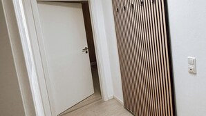 Een gang met een wand van houten latten, een deur aan het einde en een plafondlamp.