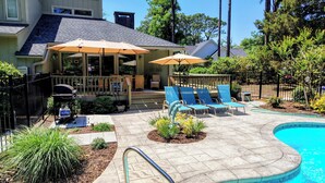 Zona junto a la piscina con sillones, sombrillas y una parrilla.