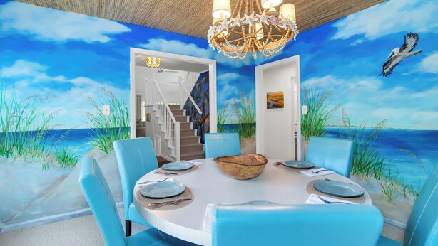 Un comedor con un mural de playa, sillas azules, una mesa redonda y una araña.