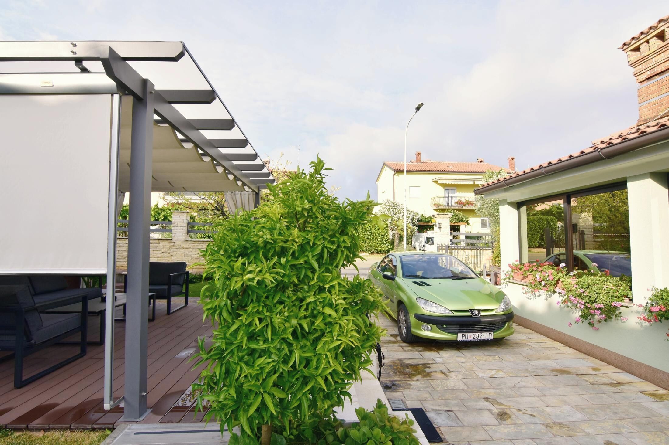 Een groene auto geparkeerd op een oprit, een overdekt terras en een gebouw met een pannendak.