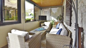 A cozy room with wicker furniture, a flat-screen TV, and a large window overlooking a garden. - Holiday home with garden and BBQ in Umag (Umag)